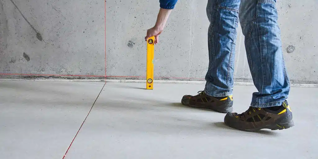 A worker checking a concrete floor's level with a measuring rod